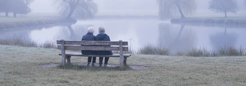 Zwei Personen sitzen auf einer Bank vor einem See