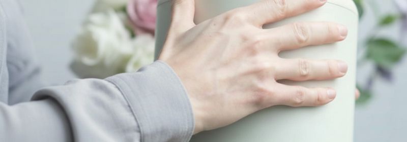 Eine Hand hält eine helle Urne