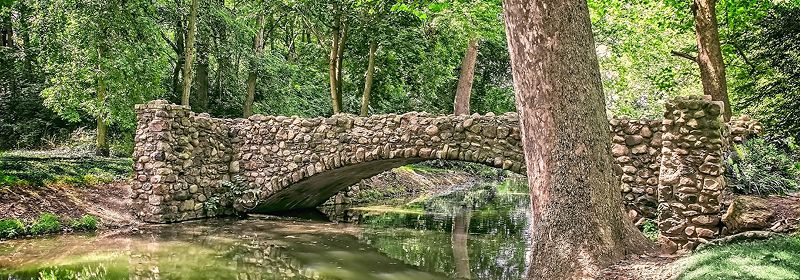Eine Steinbrücke im Wald über einen Fluss umgeben von Bäumen